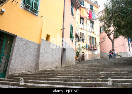 RIOMAGGIORE ITALIE - Le 24 avril 2011 ; Couple de voyageurs s'asseoir sous le té en haut des marches menant à la cuisine italienne traditionnelle et ancienne colline village appartement Banque D'Images