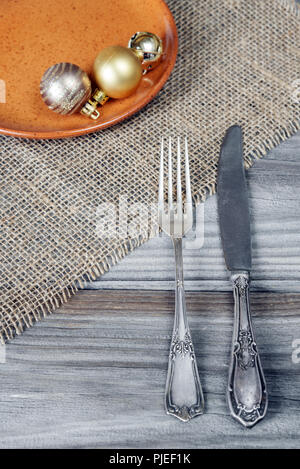 Fourchette et couteau en acier et des boules de Noël sur une plaque en céramique sont situés sur la table en bois, recouvert de tapis grossier Banque D'Images