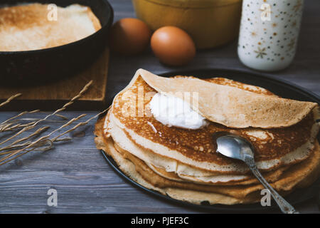 Crêpes dans une poêle et ingrédients pour eux sur une table en bois. Banque D'Images