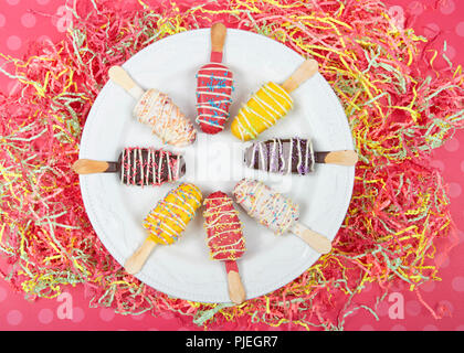 Plusieurs bonbons colorés popsicle dénudée cake pops avec saupoudre sur le dessus d'une assiette de porcelaine blanche sur fond bleu à pois rose et partie confet Banque D'Images