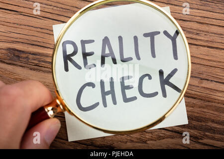 Close-up of Person's Hand voir la réalité Vérifier mot par une loupe sur un bureau en bois Banque D'Images