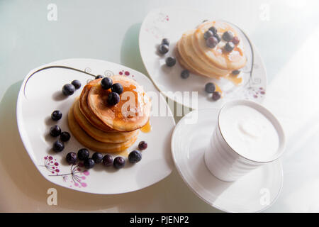 Des plaques à crêpes surmonté de sirop d'érable, la cannelle et les bleuets sur les plaques blanches avec une tasse de café délicieux garnie de crème, bain doux Banque D'Images