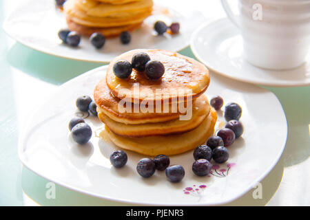 Délicieux petit tour de Crêpes avec sirop d'érable et bleuets biologiques sur la plaque blanche à côté de la tasse de café. Petit-déjeuner de crêpes sucrées Banque D'Images