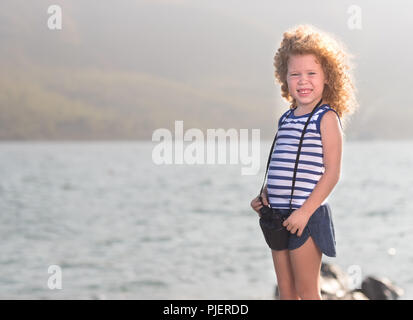 Petite fille aux jumelles, assis sur un rocher près d'une mer Banque D'Images