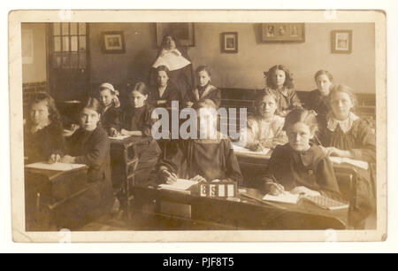 Carte postale édouardienne de junior school in classe, assis à leur bureau dans un couvent, nun en classe, vers 1910, au Royaume-Uni. Banque D'Images