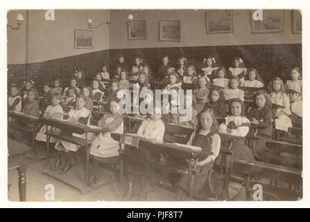 Carte postale édouardienne d'écolières assis bien droit les bras croisés chez les nourrissons ou junior school class 66, assis à leur bureau, vers 1905, au Royaume-Uni. Banque D'Images