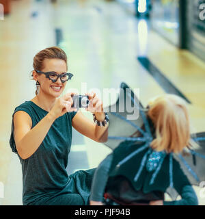 Trick or Treat. bonne mère et fille moderne à bat costume sur l'halloween à la mall avec appareil photo numérique taking photo Banque D'Images