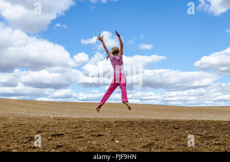 Petite fille sautant seul dans champ labouré dans la campagne pittoresque sous ciel nuageux Banque D'Images