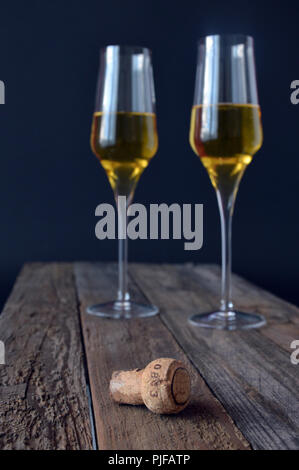 Deux verres de vin mousseux avec une capsule de bouteille sur table en bois Banque D'Images
