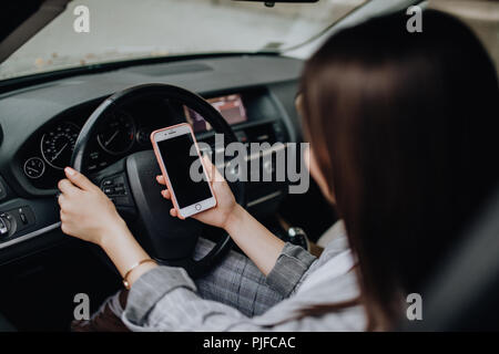 Business Woman sitting in car et en utilisant son smartphone. Immersive image avec l'écran du téléphone et la pilote Banque D'Images