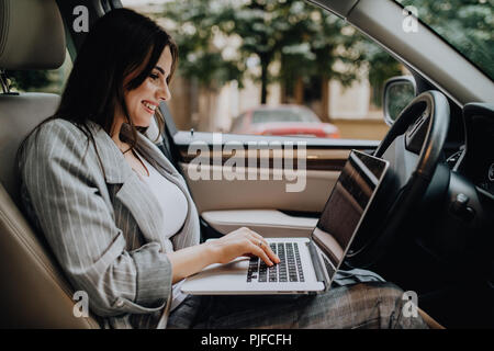 Belle jeune femme d'affaires à l'aide d'ordinateur portable et téléphone dans la voiture. Banque D'Images