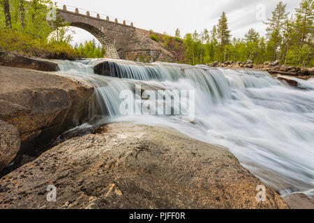 Vieux pont de chemin de fer fait de briques avec un portail, l'eau courante à partir de la rivière sous elle et forêt en arrière-plan, comté de Jokkmokk, en Laponie suédoise, Suède Banque D'Images