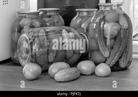 Accueil préservation : grands pots en verre rouge avec des tomates mûres et concombres, scellée. metallid Image noir et blanc. Banque D'Images