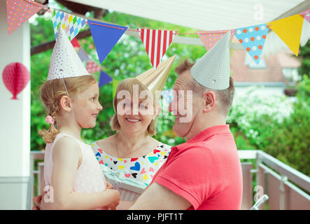 Portrait of happy grandparents celebrating birthday avec leur jolie petite-fille sur la terrasse décorée de couleurs Banque D'Images