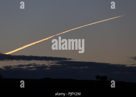 Traînée de condensation d'un avion tôt le matin par la lumière du soleil Banque D'Images