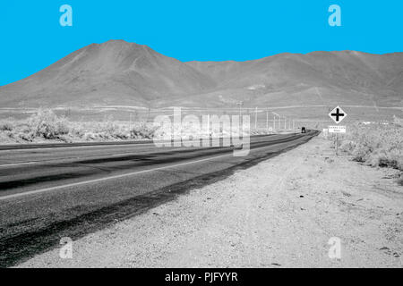 Désert solitaire l'autoroute en direction du montagnes stériles sous un ciel bleu. Banque D'Images