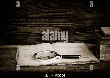 Photo en noir et blanc. Ouvrez livre ancien avec une loupe et une pile de livres sur une table en bois. Le concept de l'étude, l'étude. avec l'espace f Banque D'Images