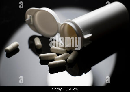 Close up of white capsules spilling out of a white medicine jar sur un tableau noir. Macro isolé de la prescription de médicaments. Banque D'Images
