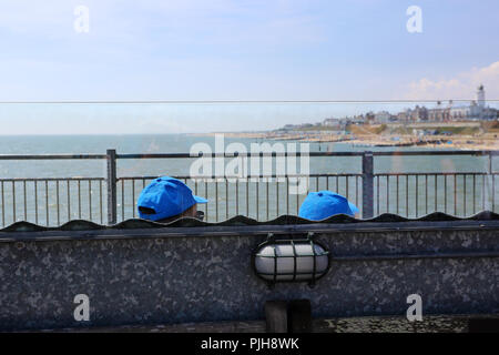 Deux personnes, reconnaissable seulement par leurs casquettes de baseball, s'asseoir sur un banc pour contempler la mer à Southwold, Suffolk, UK. Banque D'Images