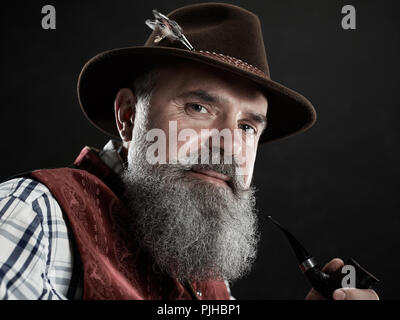 Portrait dramatique de barbu gris smiling senior man in hat fumeurs pipe. Vue sur la tyrolienne, autrichienne, vieil homme bavarois en costume traditionnel national en style rétro. Banque D'Images