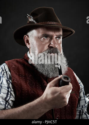 Portrait dramatique de barbu gris senior man in hat fumeurs pipe. Vue sur la tyrolienne, autrichienne, vieil homme bavarois en costume traditionnel national en style rétro. Banque D'Images