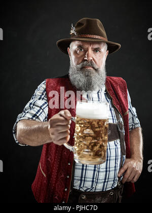 Allemagne, Berlin,. Le smiling man with beer habillé en dans le style autrichien ou en costume bavarois hat holding mug de bière au studio Banque D'Images