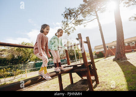 Cute little girls having fun sur une aire de jeux extérieure. Twin Sisters sautant de maisons en bois rond dans le parc aux beaux jours. Banque D'Images