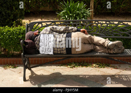 Espagne, Jerez de la Frontera, la Plaza de Abastos, sans-abri dormant sur banc, avec la mendicité signe sur l'arrière Banque D'Images