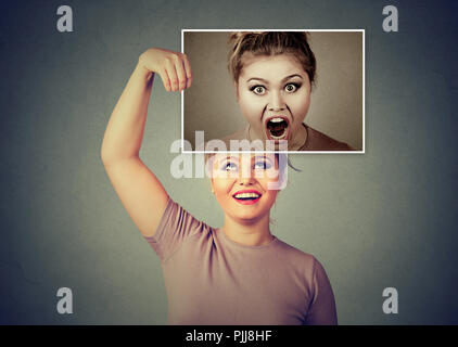 Young woman smiling tout en maintenant l'image d'elle-même dans l'humeur en colère et crier après avoir double personnalité Banque D'Images