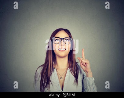 Portrait d'une femme dans les verres du doigt de maintien par avoir idée lumineuse sur fond gris Banque D'Images