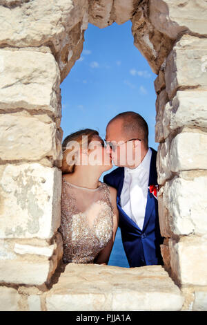 Mariage. Couple heureux jour mariage. Beaux mariés à la plage. Cheerful couple marié et permanent, baiser sur le mur de pierre. Banque D'Images