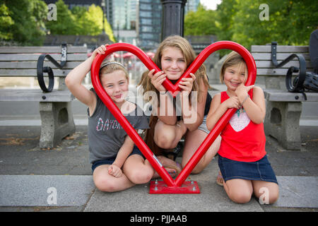 Trois smiling girls réunis autour d'une forme de coeur en métal. Vancouver, BC. Banque D'Images