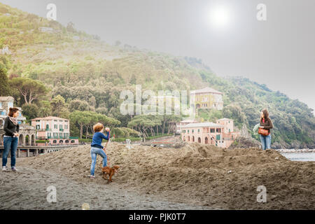 Italie LEVANTE - le 24 avril 2011 ; la lumière vive derrière littoral méditerranéen beach village situé en dessous de colline avec avec trois femmes en vacances sur dunes takin Banque D'Images