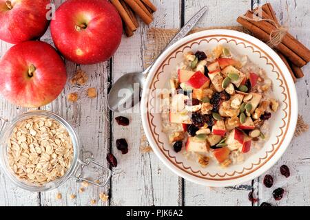 Petit-déjeuner d'automne avoine avec les pommes, les canneberges, les noix et graines, sur scène au-dessus de table en bois blanc rustique Banque D'Images