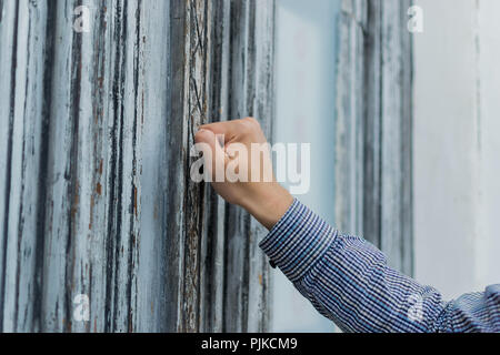 Postman main dans une chemise à carreaux frappant son poing dans le vieux et minable porte avant. Y a quelqu'un. Banque D'Images