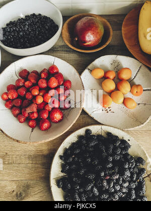 Fruits d'été frais dans des bols en céramique sur table en bois dans la cuisine. des bleuets, mangues, abricots, fraises, bananes, le mûrier à partir de zéro. Banque D'Images