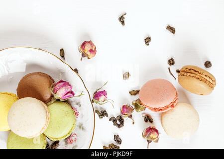 Macarons multicolores sur belle assiette de porcelaine, le thé et les boutons de rose sur fond blanc ; haut Vue, télévision lay Banque D'Images