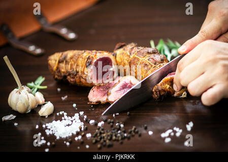 Découper une portion de rôti de bœuf biologique rouleau avec couteau sur table en bois avec de l'ail Sel et poivre à Melbourne, Australie Banque D'Images