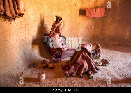 Une jeune femme Himba montre comment elle nettoie et les parfums elle-même avec l'aide de la fumée s'élevant d'un pot en argile. Banque D'Images