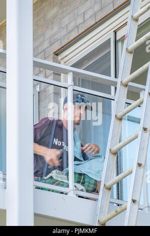 Homme nettoyant lave le verre sur le balcon d'un immeuble. Banque D'Images