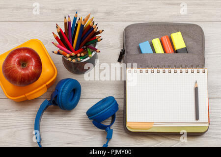 Les fournitures scolaires. Boîte à sandwich jaune, écouteurs, apple, support métallique pour crayons avec des crayons de couleurs, ouvrez un livre d'exercices sur-sac à crayons de couleur Banque D'Images