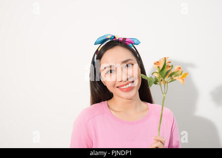 Portrait de l'adorable, belle, cute woman in casual vêtements avec sourire rayonnant et de longs cheveux blonds, tenant trois fleurs en main près de chee Banque D'Images