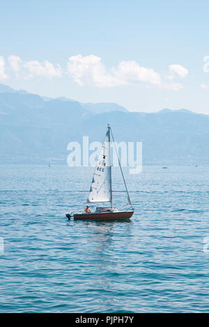 Petit voilier sur le Lac Léman (Lac de Genève) sur belle journée ensoleillée avec des montagnes et des nuages blancs sur l'arrière-plan Banque D'Images