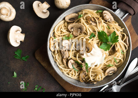 Les pâtes Spaghetti aux champignons et sauce crème sur fond rustique, vue du dessus. Les pâtes italiennes faites maison avec champignon en plat de cuisson. Banque D'Images