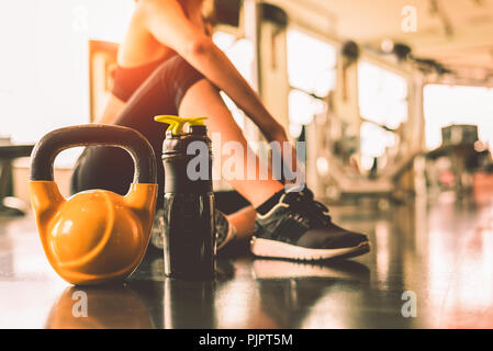 Close up kettlebells avec exercice d'entraînement dans la salle de sport femme rupture remise en forme détente après l'entraînement sportif avec des protéines bien agiter le flacon. La vie saine Banque D'Images