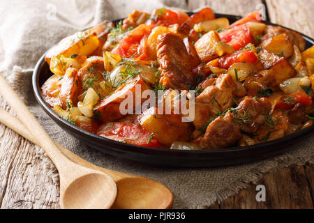 Home-style alimentaire : une viande avec pommes de terre, tomates, oignons, herbes et épices gros plan sur une poêle sur une table horizontale. Banque D'Images