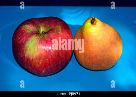 Une pomme rouge striée et une poire jaune sur un tableau bleu turquoise Banque D'Images
