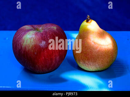 Une pomme rouge striée et une poire jaune sur un tableau bleu sur fond bleu dans close-up vue latérale. Banque D'Images