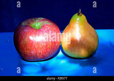 Une pomme rouge striée et une poire jaune sur fond bleu Banque D'Images