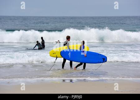 Les jeunes gens portant des planches de surf,Sennen Cove, Cornwall, Angleterre, Royaume-Uni Banque D'Images